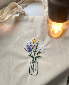 a tote bag with embroidered flowers on it and a light bulb in the background