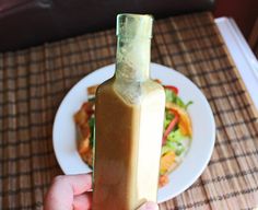 a person holding a bottle in front of a plate with food on it