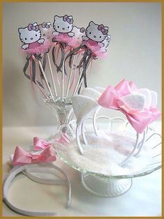 hello kitty cake toppers in a glass vase with pink bows on the stems and ribbon