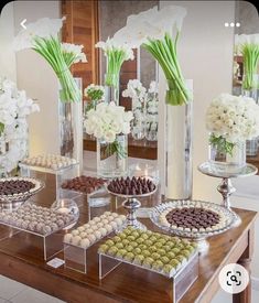 a table topped with vases filled with white flowers and chocolate covered candies next to each other