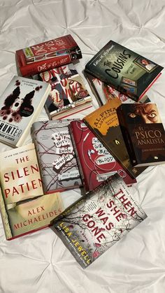 a pile of books sitting on top of a white bed covered in sheets and pillows