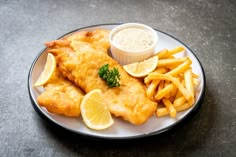 fish and fries are served on a plate with lemon wedges next to dipping sauce