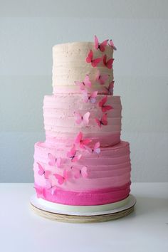 a multi layer cake with pink frosting and butterflies on top, sitting on a plate