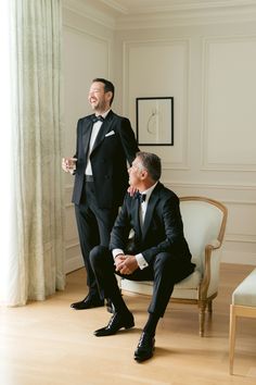 two men in tuxedos are sitting on a chair and one is holding a drink