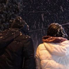 two people walking in the snow with an umbrella over their heads and one person wearing a white coat