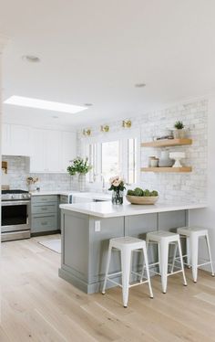 a kitchen with white and gray cabinets and counter tops, two stools in front of the island