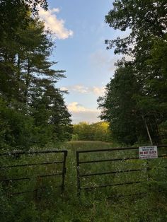 an open gate in the middle of a field with trees and grass on both sides