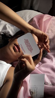 a woman laying on top of a bed holding up a piece of paper next to her face