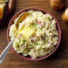 a bowl filled with mashed potatoes topped with cheese and chopped green onions next to bread