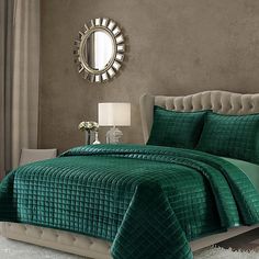 a bed with green comforter and pillows in a room next to a mirror on the wall