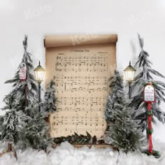 an old sheet music with christmas trees and lights in front of it on top of snow covered ground