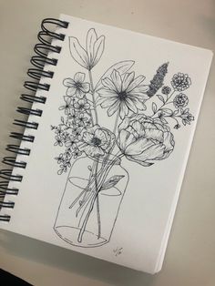 a drawing of flowers in a vase on top of a white table next to a spiral notebook