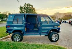 a blue truck parked on the side of a road next to a parking lot filled with cars