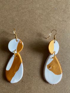 two white and brown earrings on top of a table next to each other with gold accents