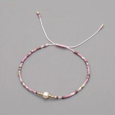 a pink and white beaded bracelet with a pearl on the end, sitting on a gray surface