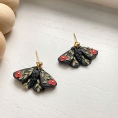 a pair of black and gold earrings with red flowers on them next to some eggs