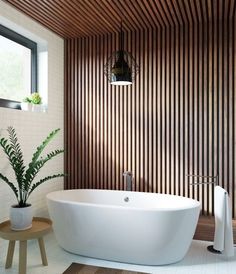 a large white bath tub sitting next to a plant in a bathroom under a window