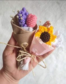 two small crocheted flowers are tied to some paper and placed in someone's hand