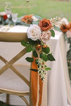 an arrangement of flowers sits on the back of a chair at a table with white linens and greenery