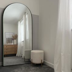 a mirror sitting on the side of a wall next to a white chair and ottoman