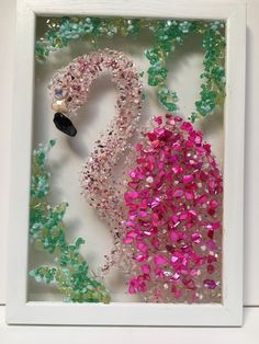 a white frame with pink, green and purple beads in the shape of a flamingo