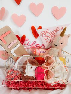 a basket filled with stuffed animals on top of a white bed covered in pink hearts