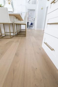 an empty kitchen with white cabinets and wood flooring, along with wooden dining chairs