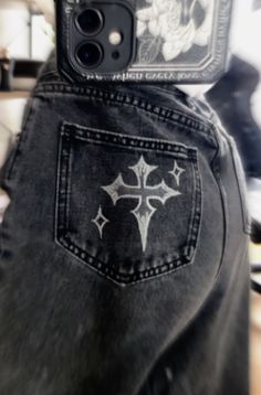 someone is holding their cell phone up to the back of his jean pants, which has an image of a cross on it