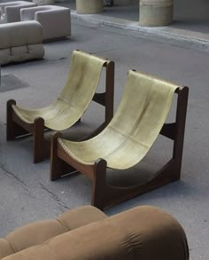 two wooden chairs sitting next to each other on top of a cement floor near couches