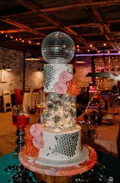 a three tiered cake decorated with flowers and disco ball decorations is displayed on a table