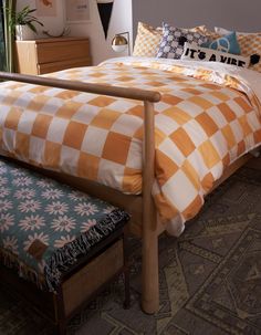 a bed with an orange and white checkered comforter next to a wooden bench