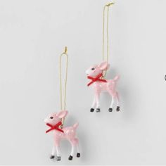 two pink ornaments with red bows hanging from the strings on a white background, one is shaped like a poodle and the other is shaped like a lamb