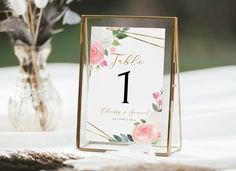 the table numbers are displayed in front of a vase with pink flowers and greenery