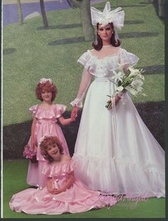 two women and a girl in pink dresses standing next to each other on the grass