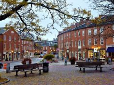 an empty street with benches and tables in front of red brick buildings on either side