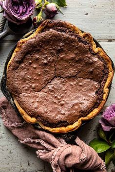 a chocolate pie sitting on top of a wooden table next to flowers and a fork