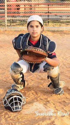 a young boy in catchers gear holding a baseball mitt on a dirt field