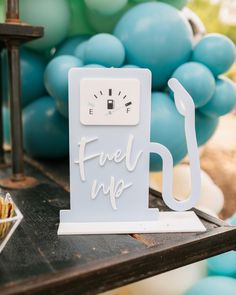 a fuel pump sign sitting on top of a table next to blue and green balloons