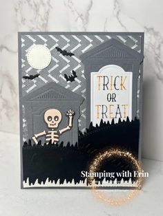 a trick or treat halloween card with a skeleton and graveyard scene in the background, on a marble surface