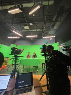 a green screen studio with camera equipment and people in the background on laptops sitting at a table