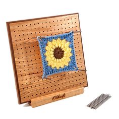 a crocheted sunflower sits on top of a piece of wood with pins