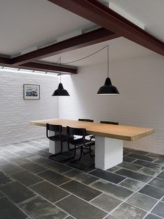 a table and chairs in a room with white walls, exposed beams and black pendant lights