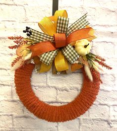 a knitted wreath hanging on the side of a white brick wall with an orange and yellow bow