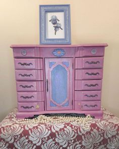 a pink dresser sitting on top of a bed next to a framed picture above it