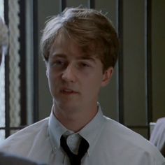 a young man wearing a white shirt and black tie in front of a mirror looking at his reflection