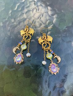 These dragon drop earrings are so much fun! Made with gold tone antique dragons. Lavender and lime green AB crystals along with a crescent moon dangle from its curled tail.  Large, bold and light weight. These are perfect for a fan of fantasy creatures.  They have about a 2.5 inch drop with simple ear wires. Beautiful statement earrings unlike any you have ever seen. Fantasy Dangle Earrings For Festival, Fantasy Festival Dangle Earrings, Gold Fantasy Earrings As Gift, Fantasy Gold Earrings For Gift, Gold Handmade Fantasy Earrings, Magical Gold Nickel-free Jewelry, Gold Fantasy Earrings For Gift, Handmade Gold Fantasy Earrings, Gold Fantasy Handmade Earrings