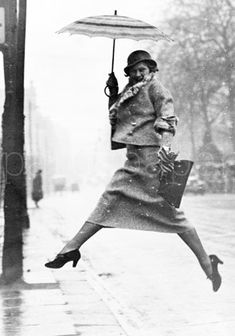 a woman jumping in the air while holding an umbrella over her head on a rainy day