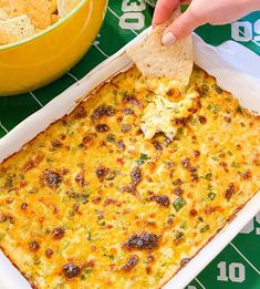 a person dipping a tortilla chip into a casserole dish with cheese and broccoli