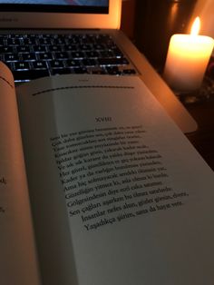 an open book sitting in front of a laptop computer on a desk next to a lit candle