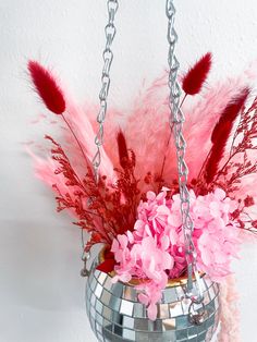 a mirror ball hanging from a chain with pink flowers and feathers in the bottom half